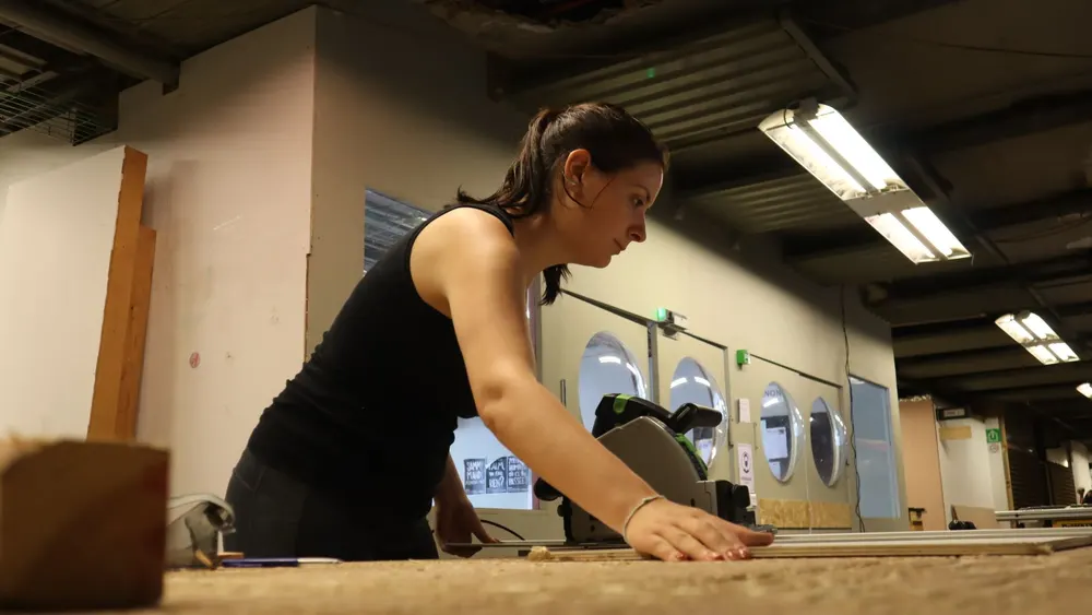 Menuisière découpant une planche à la scie plongeante dans son atelier