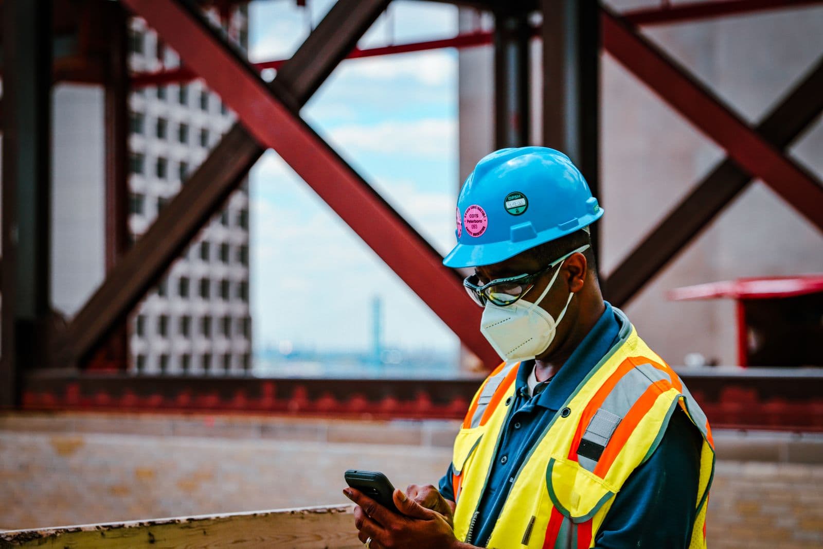 Ouvrier du bâtiment en casque et gilet haute visibilité consultant son smartphone sur un chantier