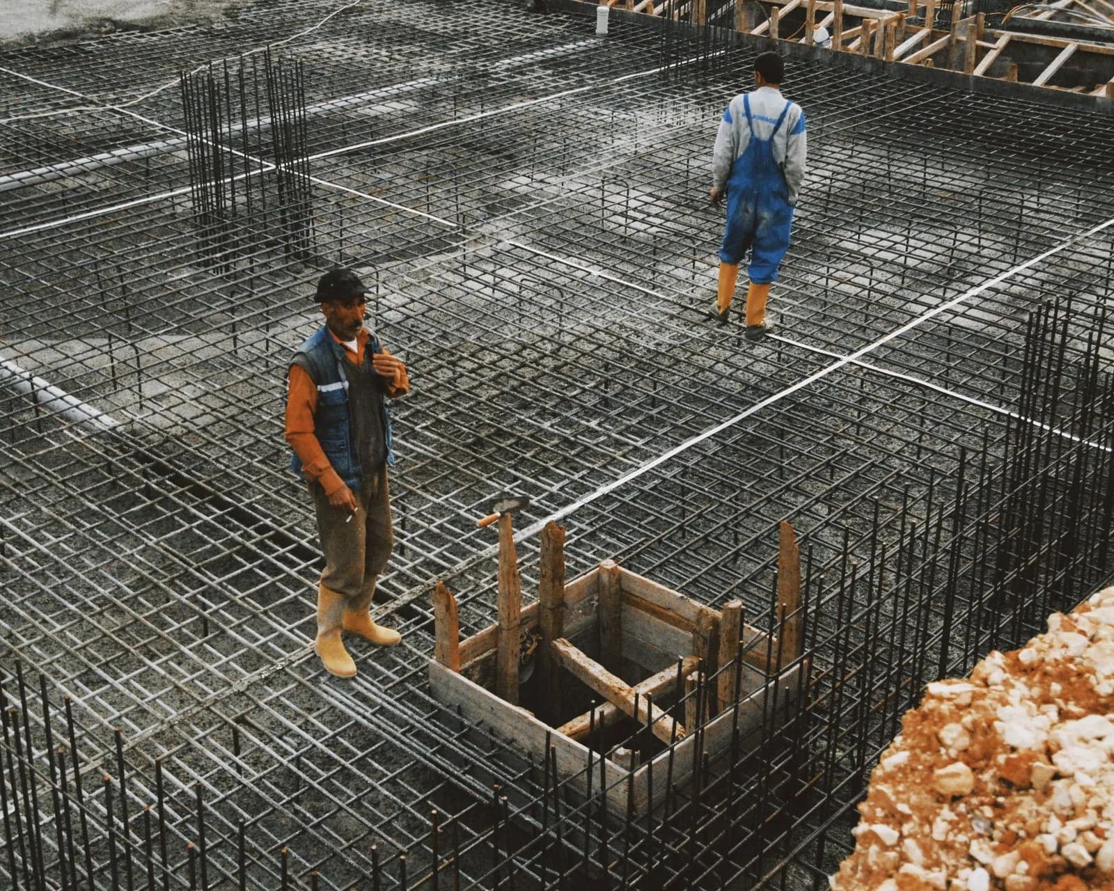 Ouvriers sur le ferraillage d'une fondation en béton armé, avant le coulage